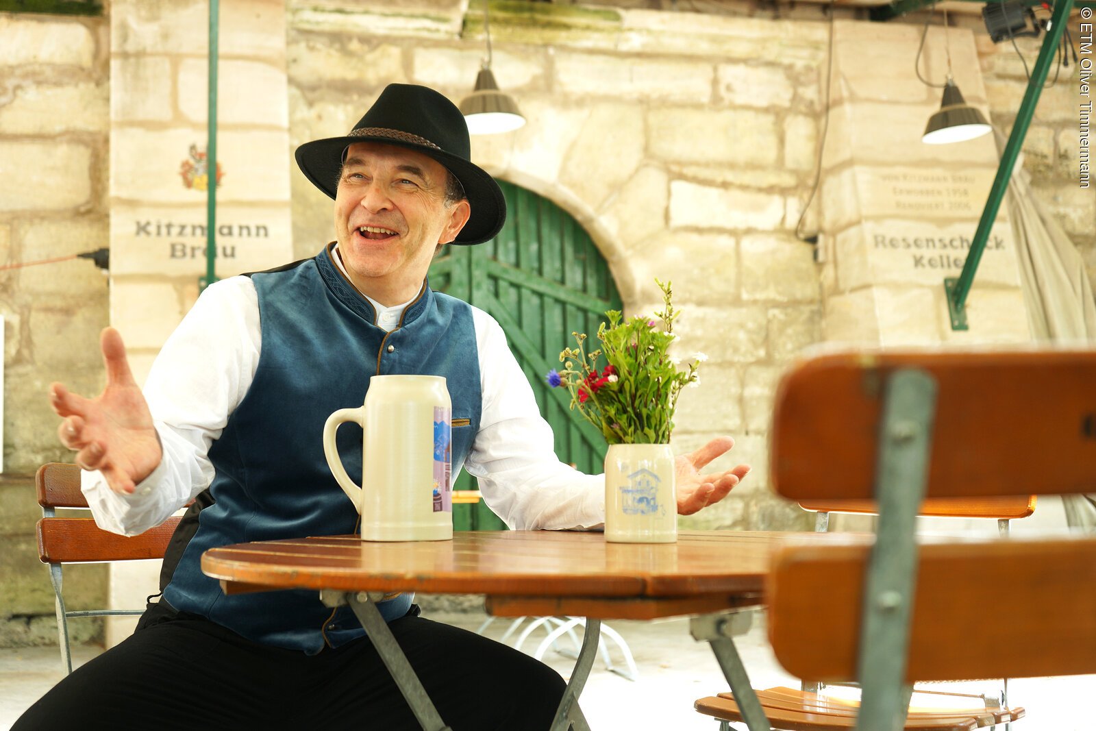 Wir sehen den kost&uuml;mierten Stadtf&uuml;hrer als Bierkutscher Schorsch, sitzend vor dem Kitzmann Keller in Erlangen, stilecht mit einem Ton-Bierkrug.
