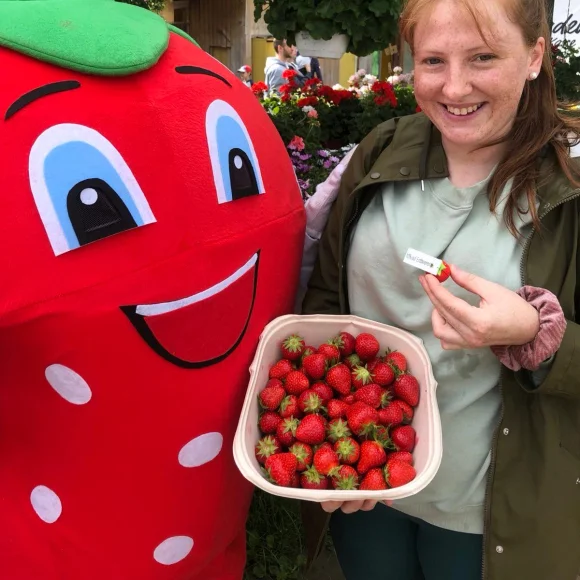 Erdbeermaskottchen und eine Frau hält Erdbeeren